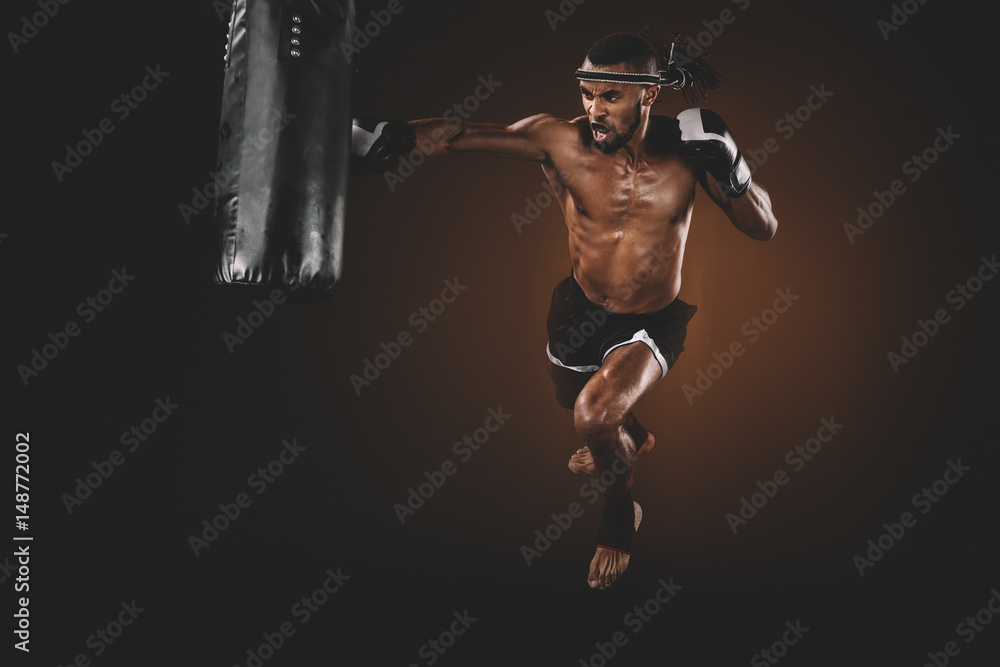 Naklejka premium angry muay thai fighter practicing punch on punching bag, action sport concept