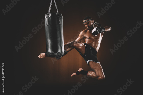 side view of focused muay thai fighter practicing kick on punching bag, action sport concept photo