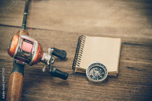 Fishing tackle - Baitcasting Reel, book and compass on wooden background
