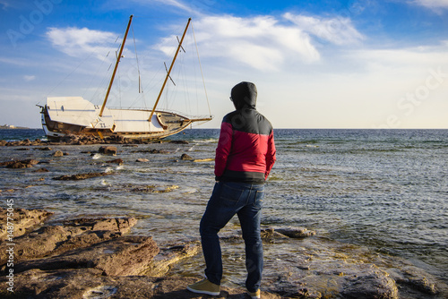 Obraz na plátně A man look the shipwrecked Boat in Calasetta, on the coast of south Sardinia whe