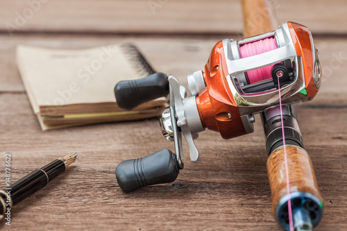 Fishing tackle - Baitcasting Reel, book on  wooden background photo