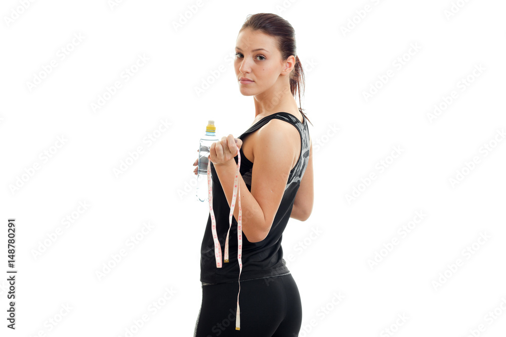 young beautiful sport girl stands with his back to the camera and keep the measuring tape and water young beautiful sport girl stands with his back to the camera and keep the measuring tape and water