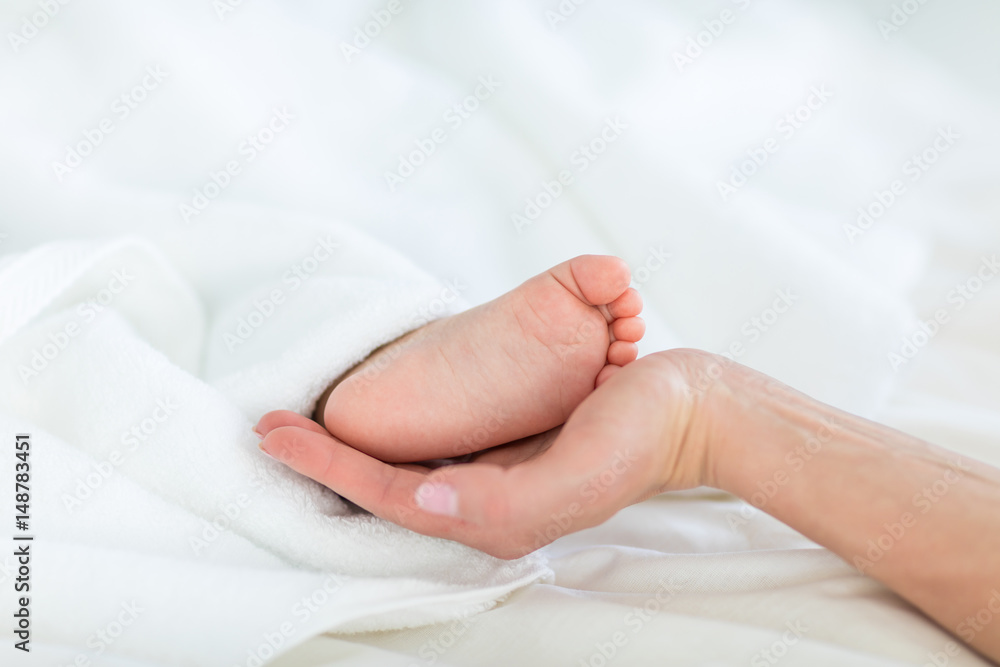 Close-up partial view of mother holding foot of child lying under blanket, 1 year old baby concept Close-up partial view of mother holding foot of child lying under blanket, 1 year old baby concept