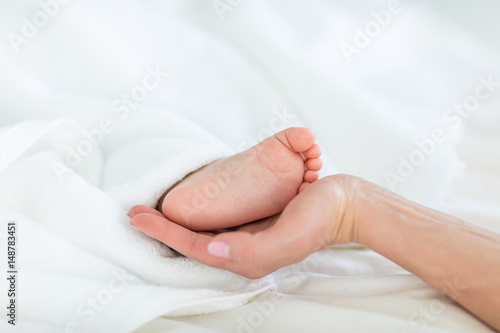 Close-up partial view of mother holding foot of child lying under blanket, 1 year old baby concept