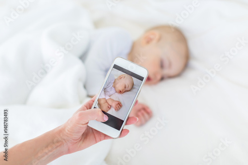 Close-up partial view of mother photographing adorable sleeping son with smartphone, 1 year old baby concept