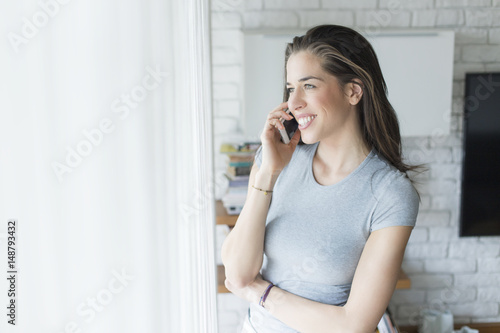 Morning scene. Beautiful woman using cell phone next to the window