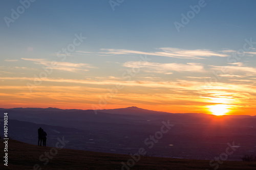 A boy and a girl looking at sunset from the top of a mountain