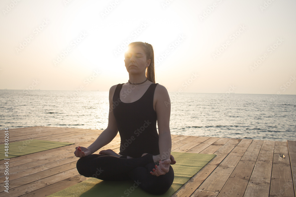 Portrait of young woman meditating on the beach, sunrise background