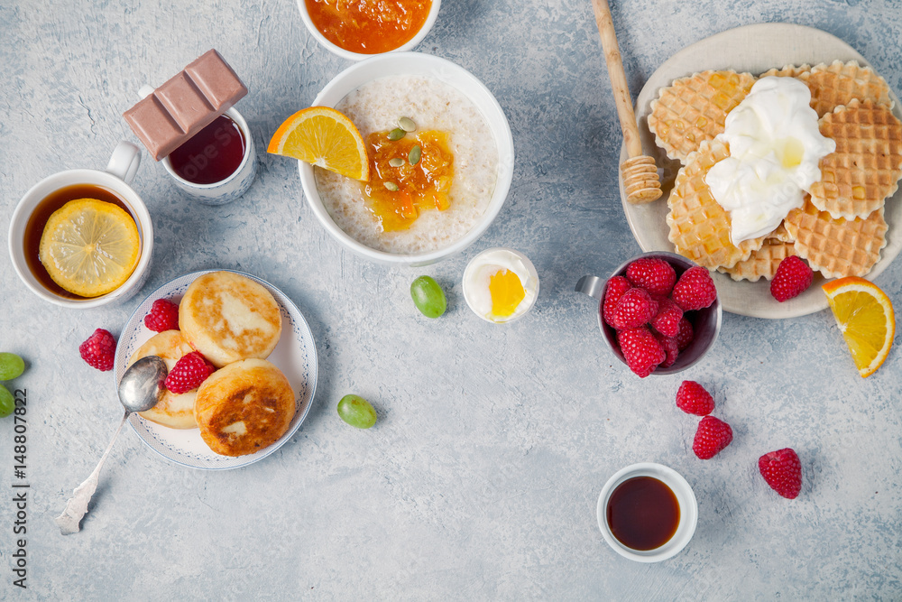 Morning atmosphere. Healthy breakfast with porridge, oatmeal, pancakes, lots of berries and snacks on blue rustic background. Morning atmosphere. Healthy breakfast with porridge, oatmeal, pancakes, lots of berries and snacks on blue rustic background.