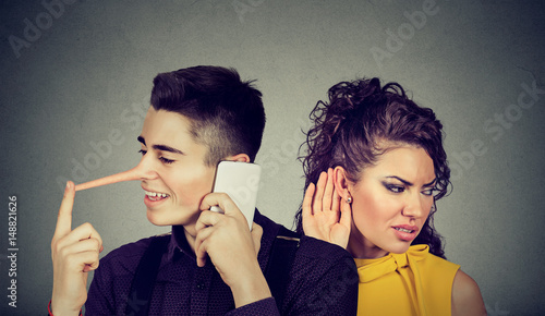Curious worried woman secretly listening to a happy man liar talking on mobile phone with his lover photo
