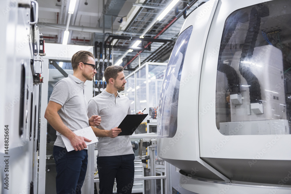 Two men looking at machine in factory shop floor Two men looking at machine in factory shop floor