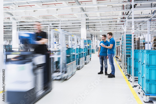 Wallpaper Mural Two men with tablet talking in industrial hall while man driving a tugger train Torontodigital.ca