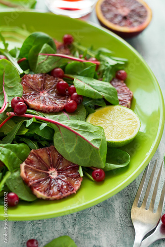 Fresh spring salad with arugula, beet leaves, avocado, red orange slices and cranberry on wooden table. Selective focus