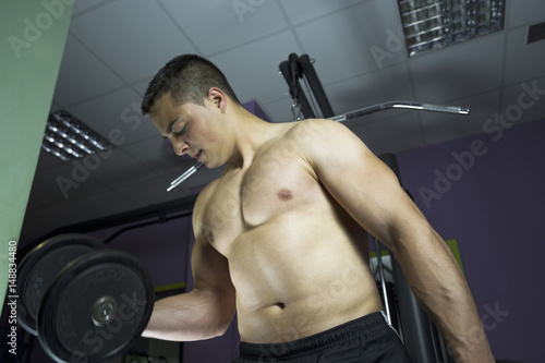 Young and fit male model posing his muscles. Muscular and fit young bodybuilder guy doing exercises with dumbbell.