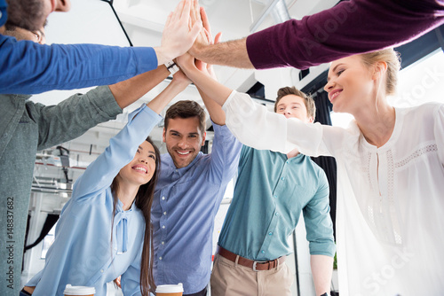 Фотография business team giving highfive together on workplace in office, young professiona