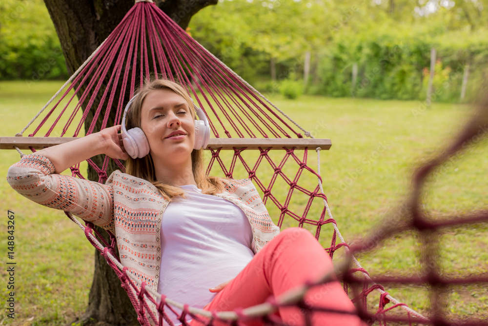 Close up portrait of woman lying down on hammock listening to music with cell phone
