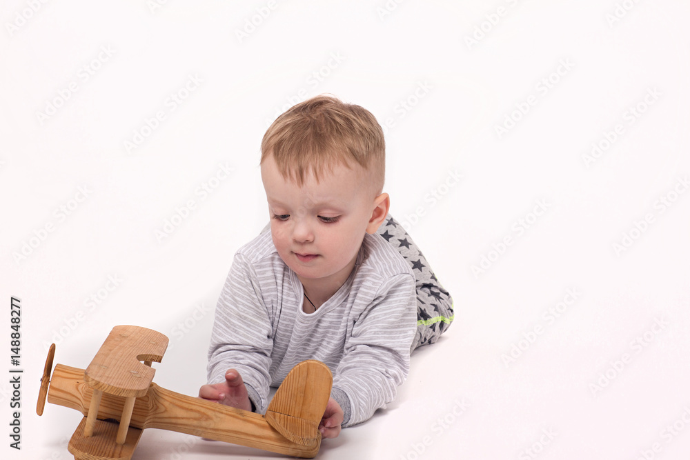 The boy is playing with a wooden plane. Isolated background The boy is playing with a wooden plane. Isolated background