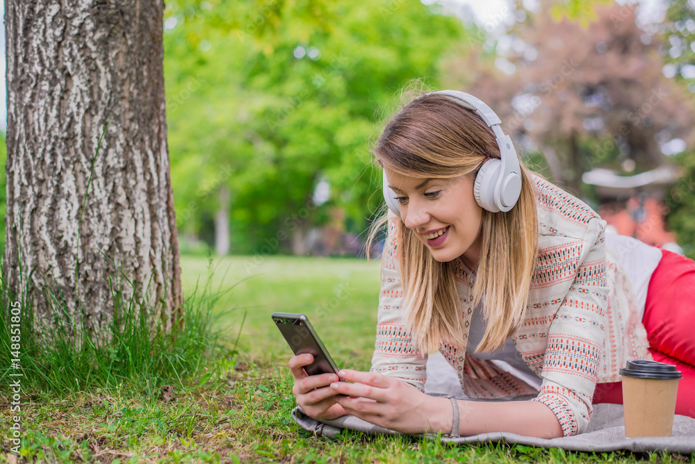 Fototapeta premium Relaxed woman listening to the music with headphones lying on the grass