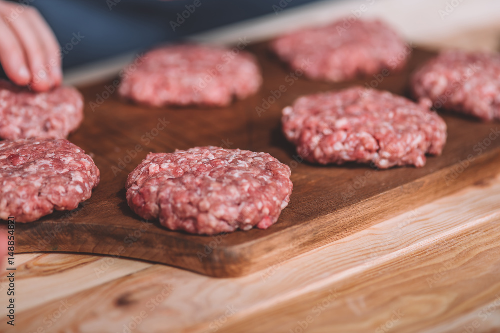 close up view of raw meat patties for burgers on wooden cutting board
