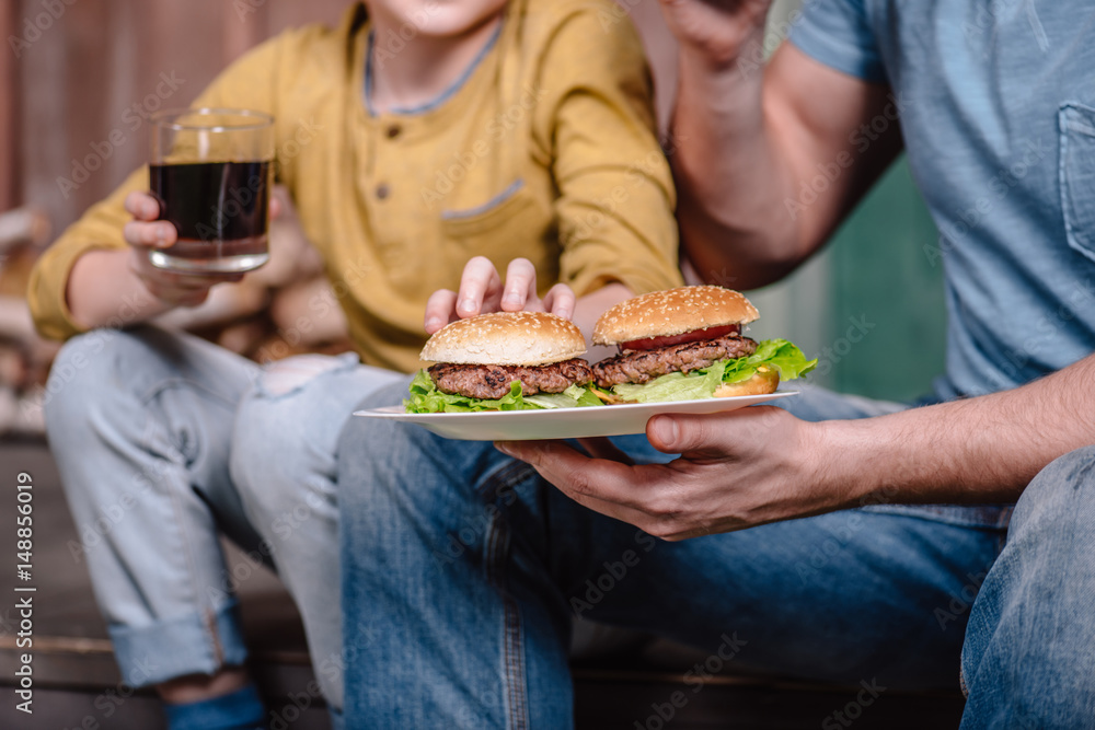 partial view of father and son holding plate with homemade burgers