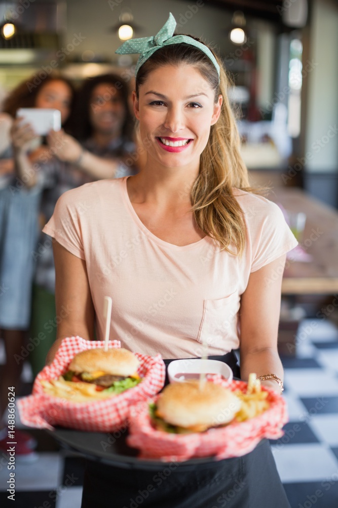 Happy waitress serving burgers in restaurant