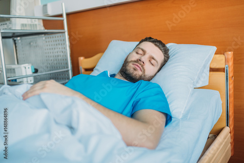 young sick man sleeping on hospital bed at ward, hospital patient bed