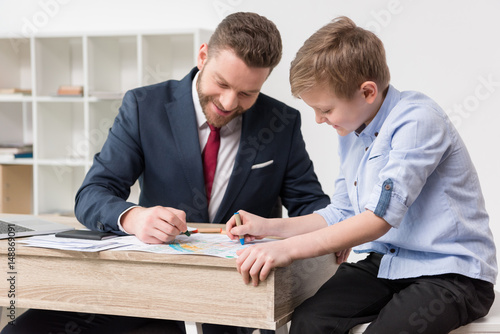 Businessman drawing on business papers with son at office