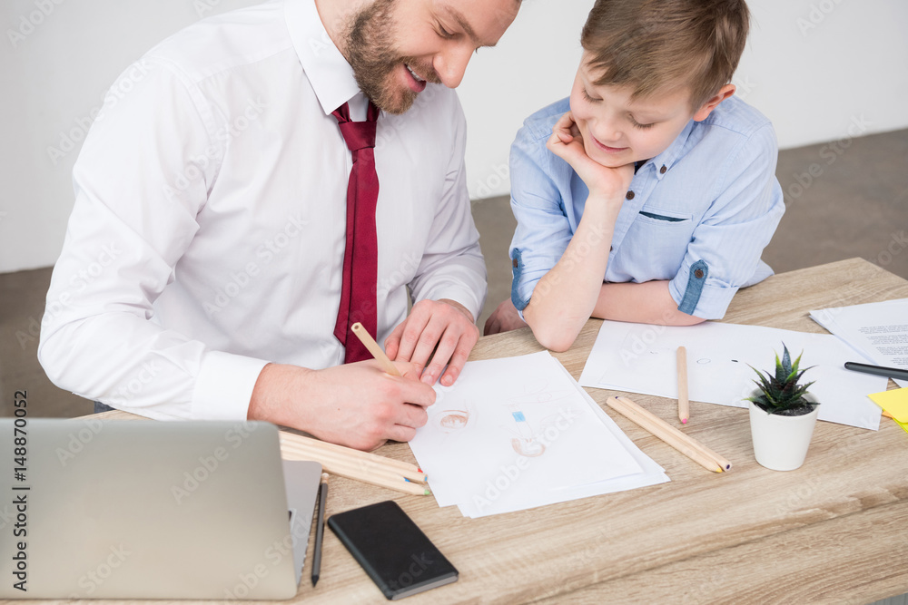 Businessman with son drawing at table in office Businessman with son drawing at table in office