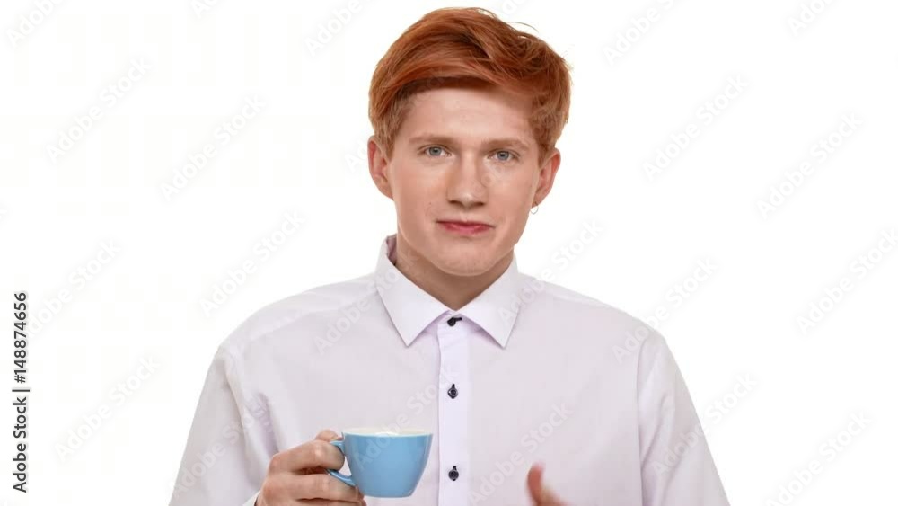 Young Caucasian redhead man drinking coffee from blue cup and showing ok on white background Young Caucasian redhead man drinking coffee from blue cup and showing ok on white background