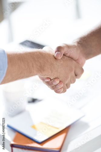 Top view of businessmen shaking hands above table with papers, business teamwork concept