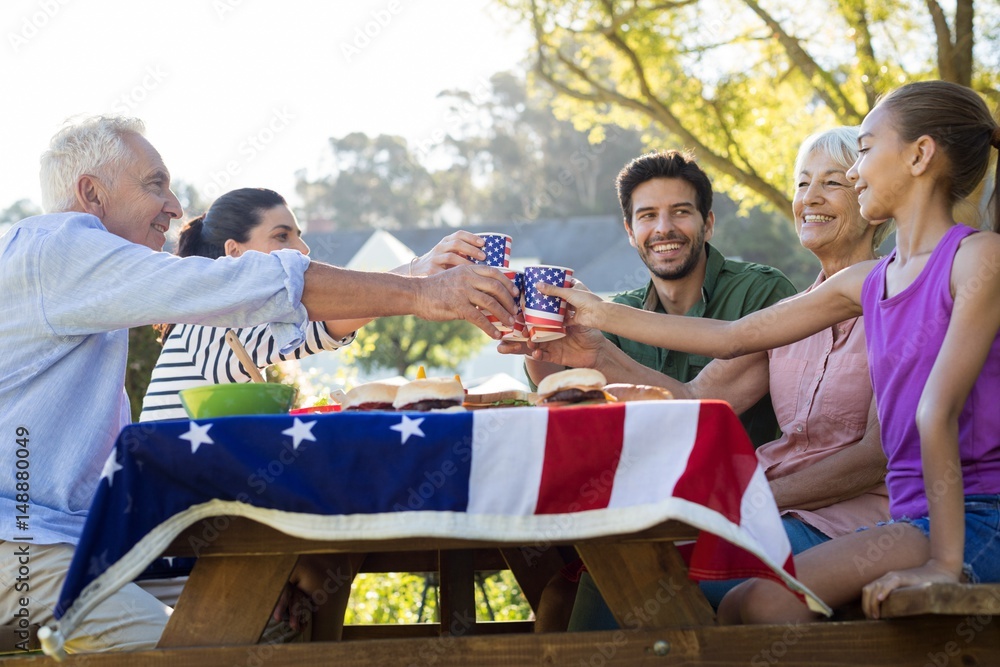 Obraz premium Happy family toasting the cups while having meal in the park