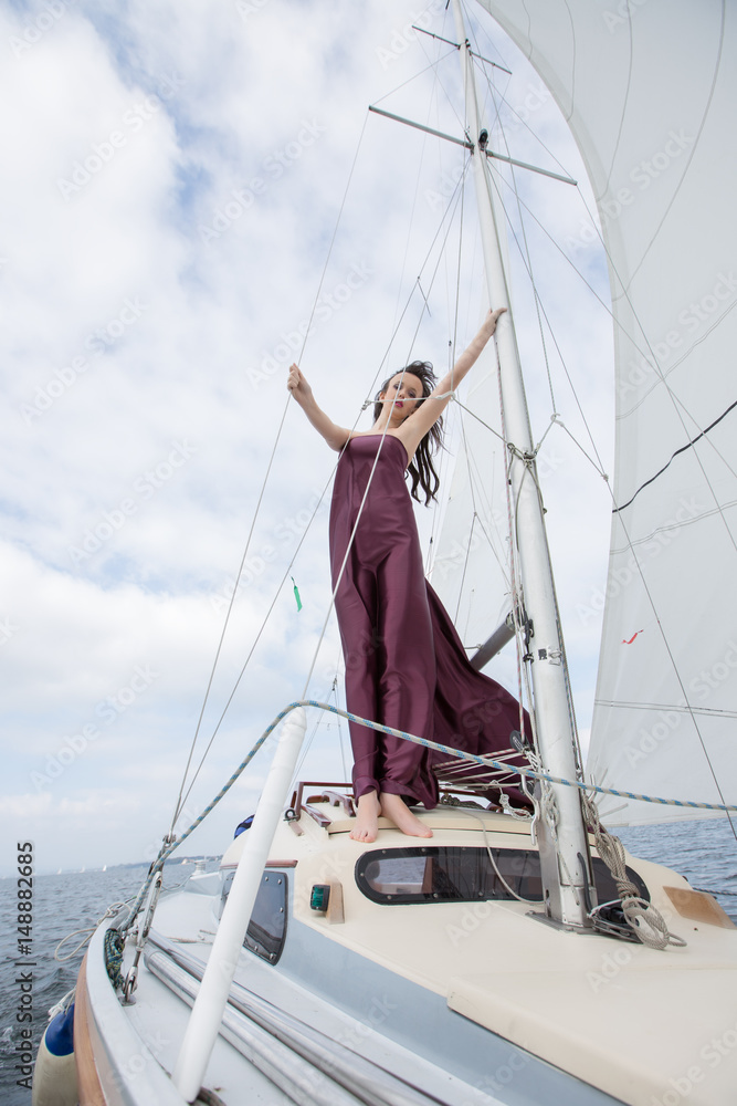 Cute brunette on a yacht in a red cherry dress, on the sea in sunny light weather