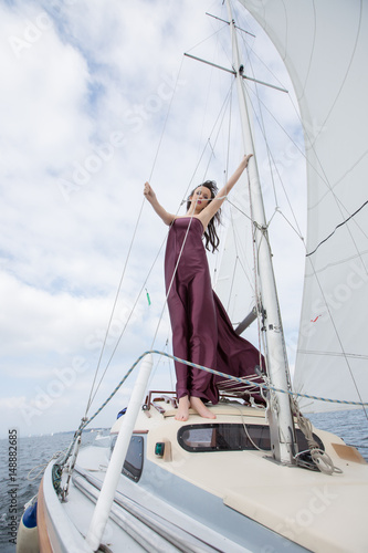 Cute brunette on a yacht in a red cherry dress, on the sea in sunny light weather © Evgeni Schemberger