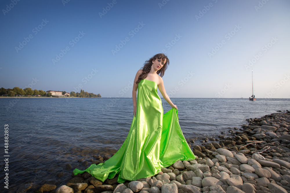 Portrait Cute brunette on the beach in a green dress, at the sea in sunny light weather Portrait Cute brunette on the beach in a green dress, at the sea in sunny light weather