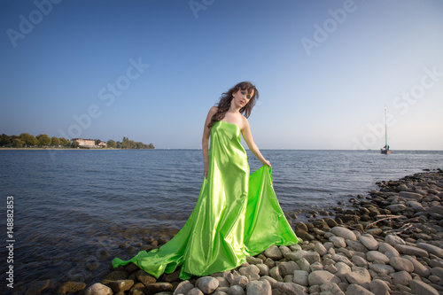 Portrait Cute brunette on the beach in a green dress, at the sea in sunny light weather
