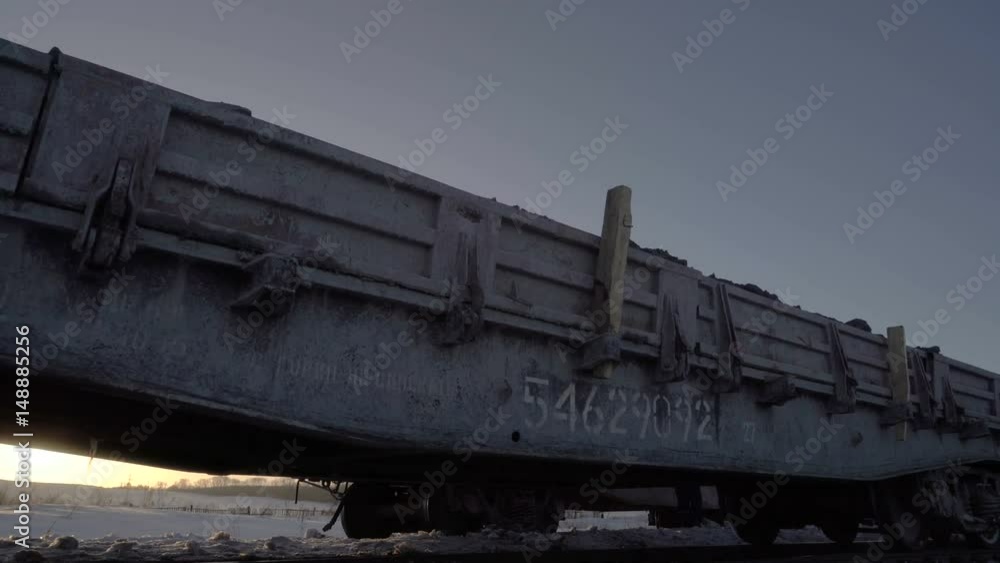 Low angle view of diesel locomotive with gondola cars moving by rail near the railroad switch against the sun in winter period. Low angle view of diesel locomotive with gondola cars moving by rail near the railroad switch against the sun in winter period.