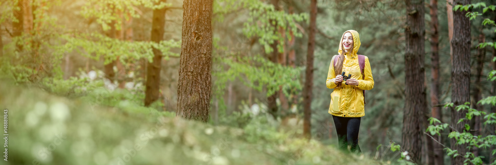 Landscape view on the pine forest with woman hiking in yellow raincoat. Cropped image for wide format Landscape view on the pine forest with woman hiking in yellow raincoat. Cropped image for wide format