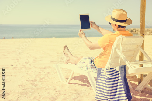 Back view of man sitting using touch screen tablet pc. Beach sunny seaside outdoors background. Travel lifestyle modern business connectivity, selfie photography, online shopping or playing game