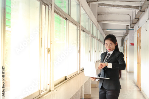 Wallpaper Mural business woman in black suit and tie look at watch on left hand and hold laptop with right hand Torontodigital.ca