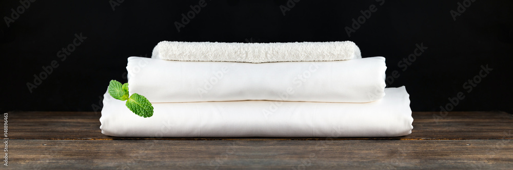 Stack of white clean new bed sheets on wooden desk against black background. Copy space. Concept of comfortable and stylish rest and dream. Stack of white clean new bed sheets on wooden desk against black background. Copy space. Concept of comfortable and stylish rest and dream.
