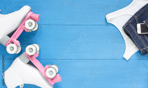 Sport, healthy lifestyle, roller skating background. White roller skates, girl clothing set, cell phone. Flat lay, top view.