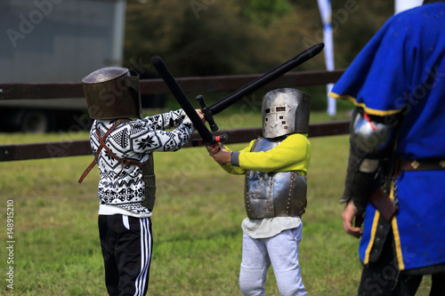 Dwaj mali chłopcy w zbrojach rycerskich walczą na miecze.