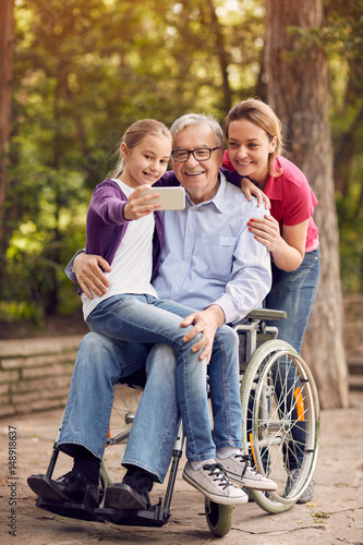family selfie time- granddaughter, daughter and disabled man in wheelchair . © luckybusiness
