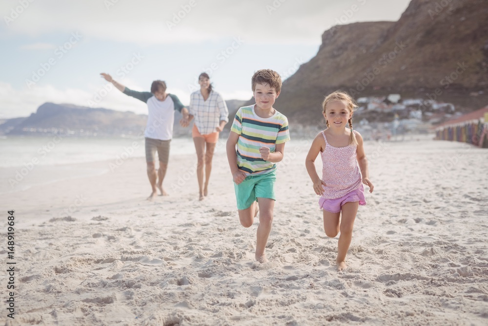Siblings running on sand with parents in background