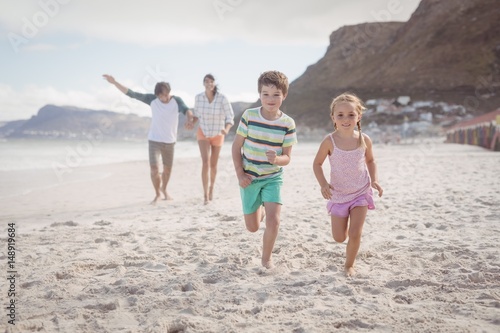 Siblings running on sand with parents in background