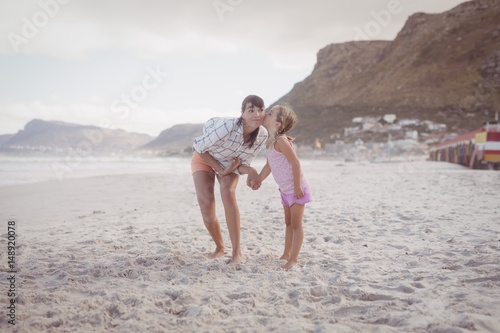 Girl kissing her mother standing at beach