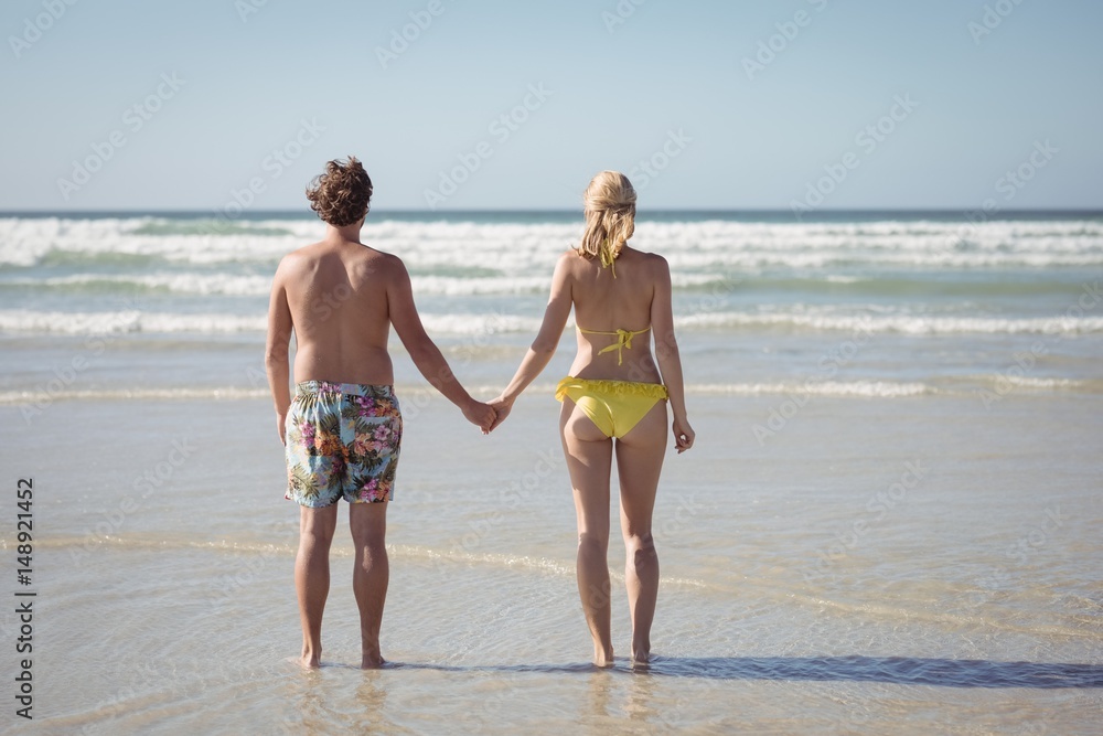 Rear view of couple holding hands while standing at beach Rear view of couple holding hands while standing at beach