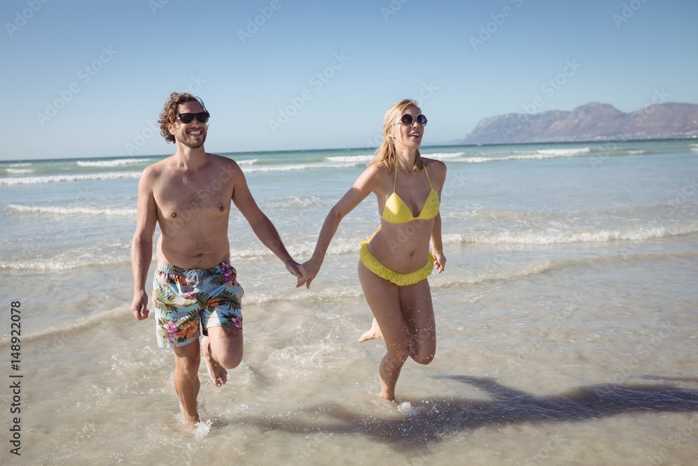 Happy young couple holding hands while running at beach