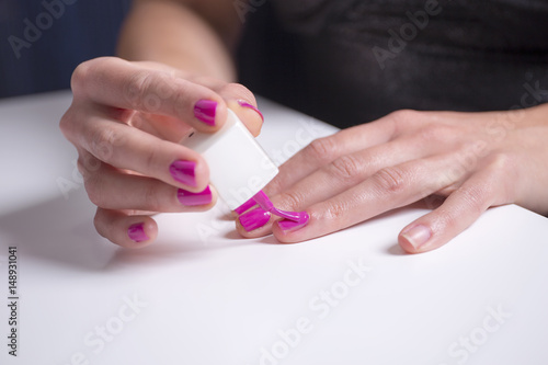 Girl paints her nails with pink nail polish