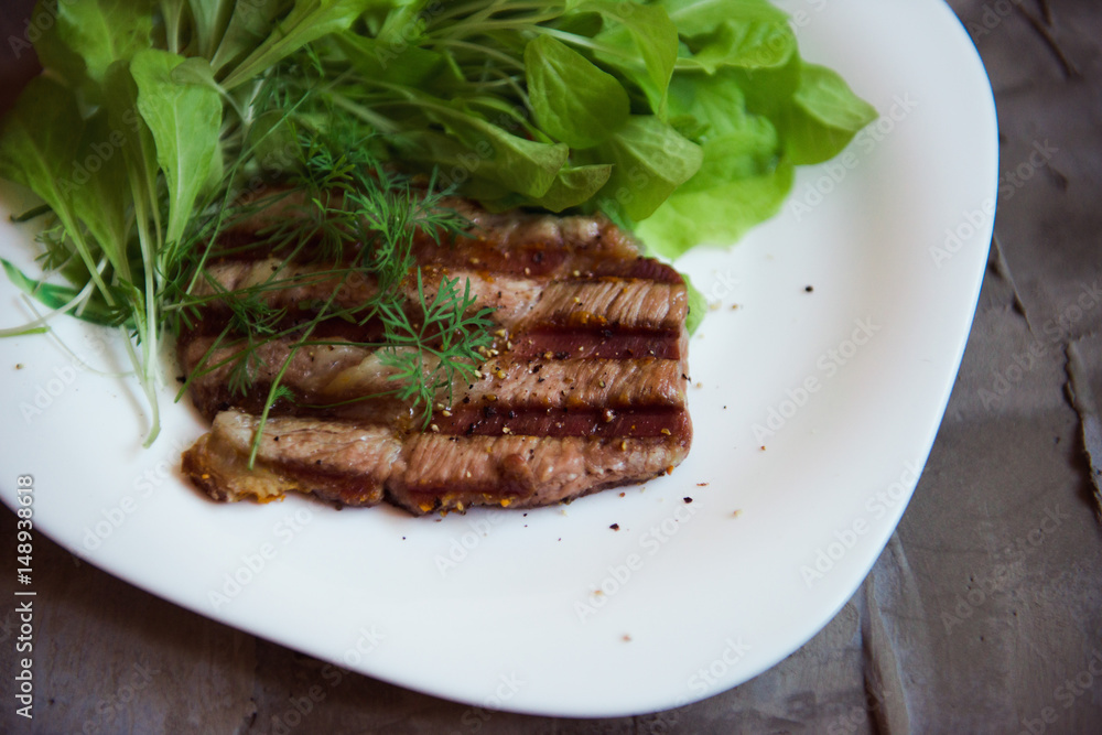 grilled piece of pork with fresh greeny on the white plate